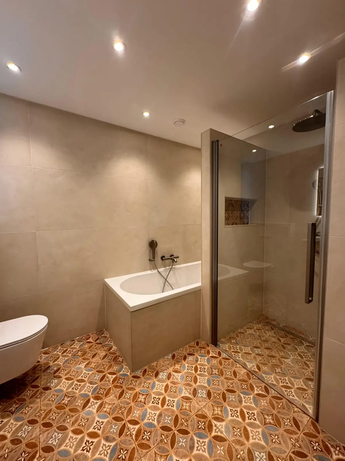 Ligbad en douche naast een vloer met warme patroontegels