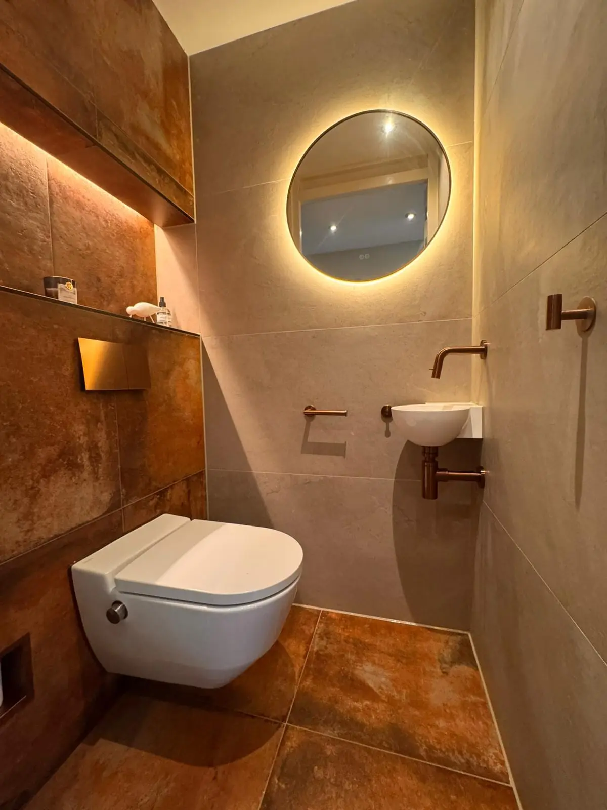 Toiletruimte met ronde verlichte spiegel en natuurkleurige tegels