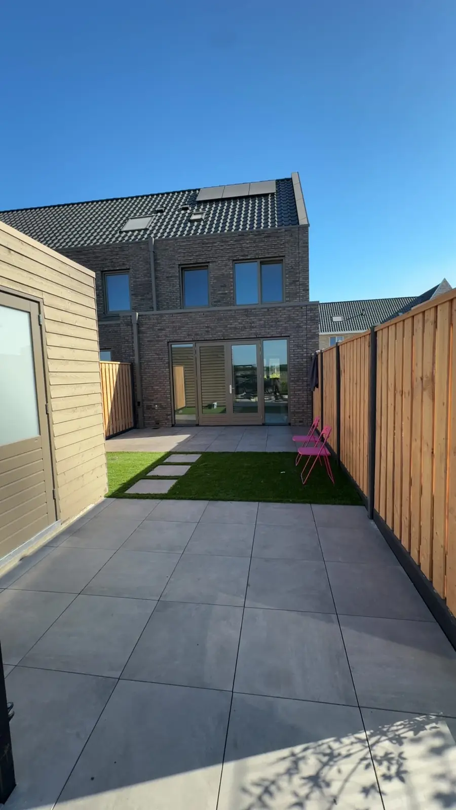 Overzicht van de nieuwbouwtuin met terras, kunstgras en schutting