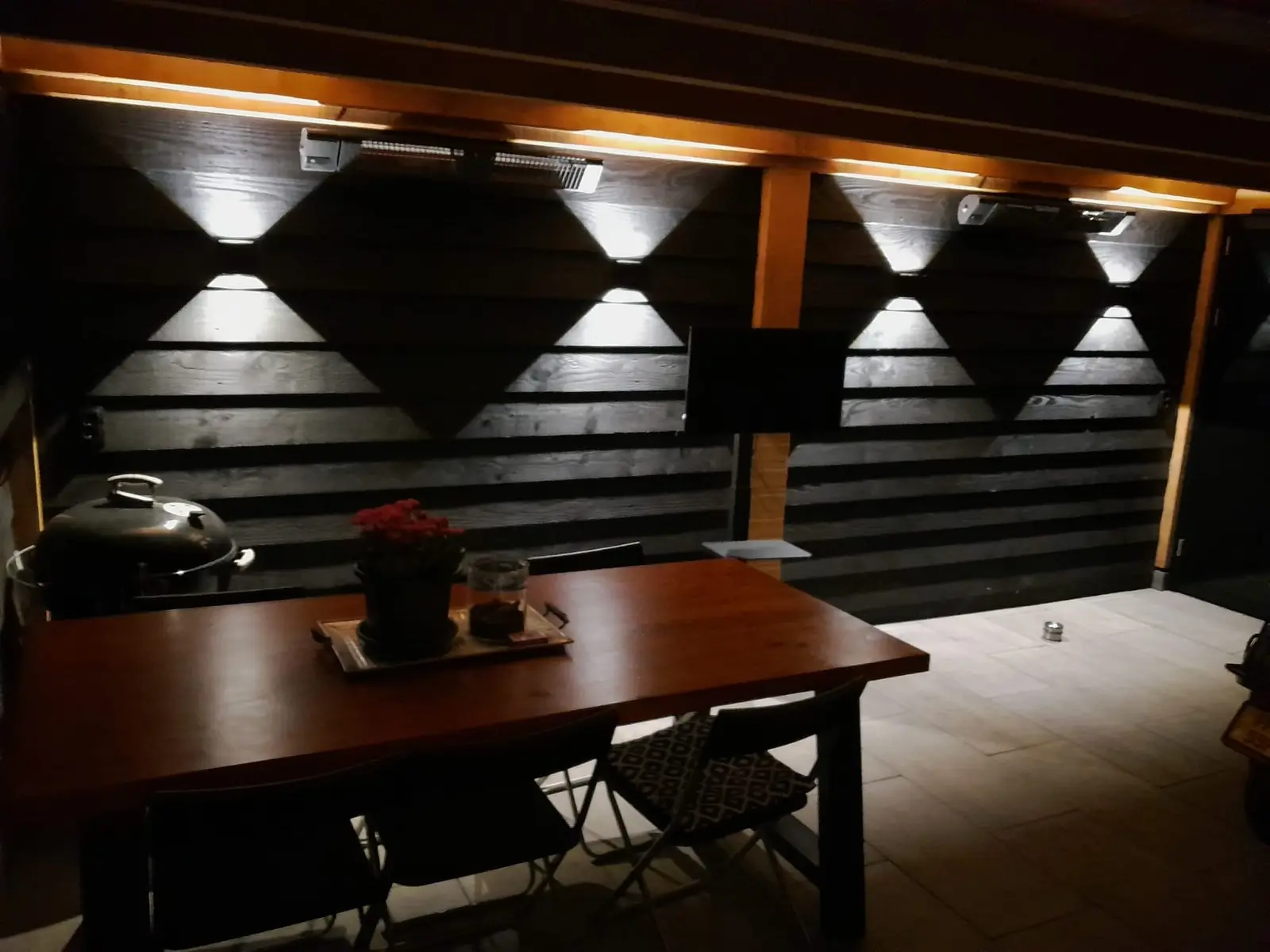 Eettafel onder de houten overkapping met wandverlichting