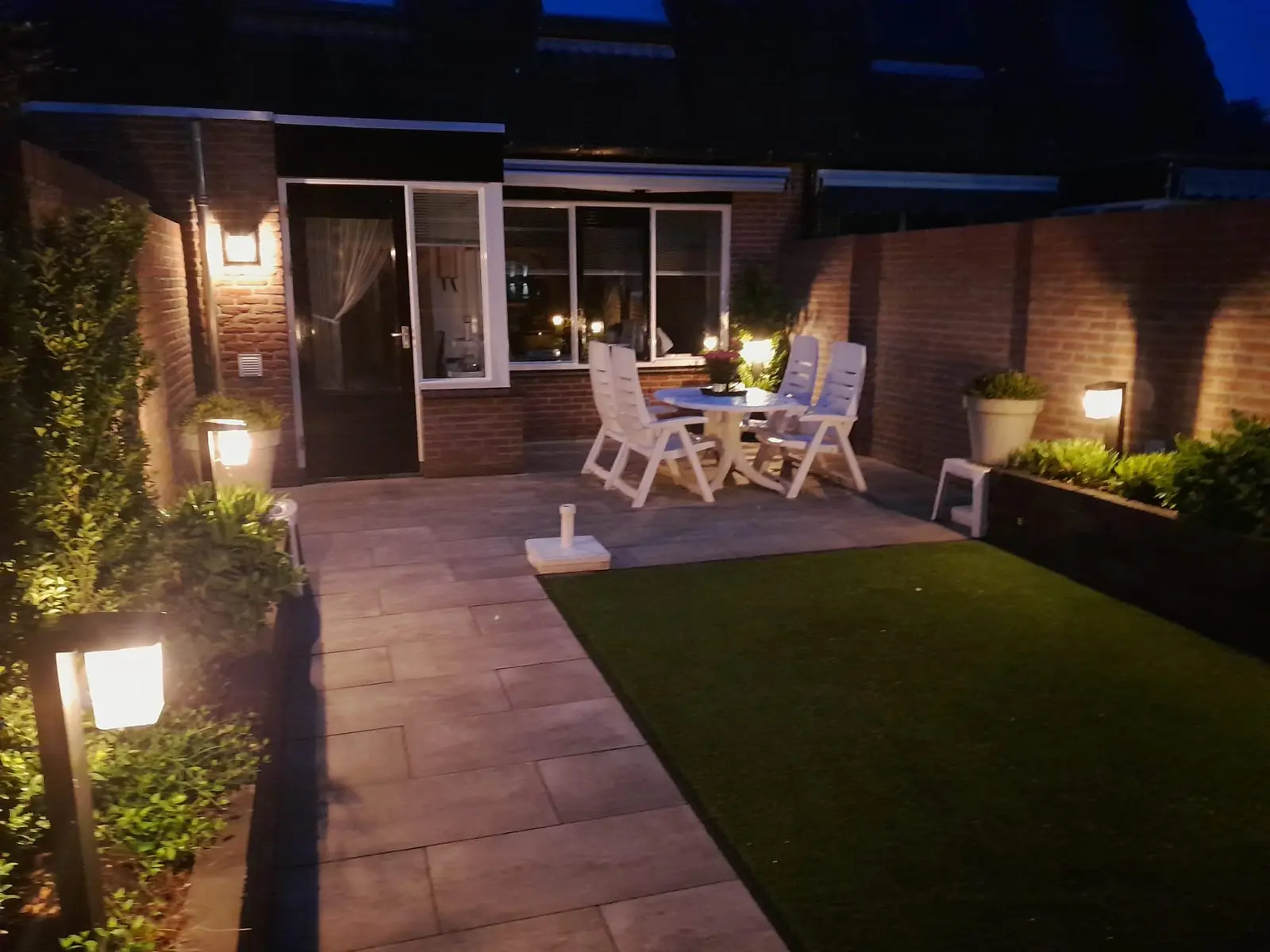 Tuin in de avond met terras aan de woning en verlichte borders