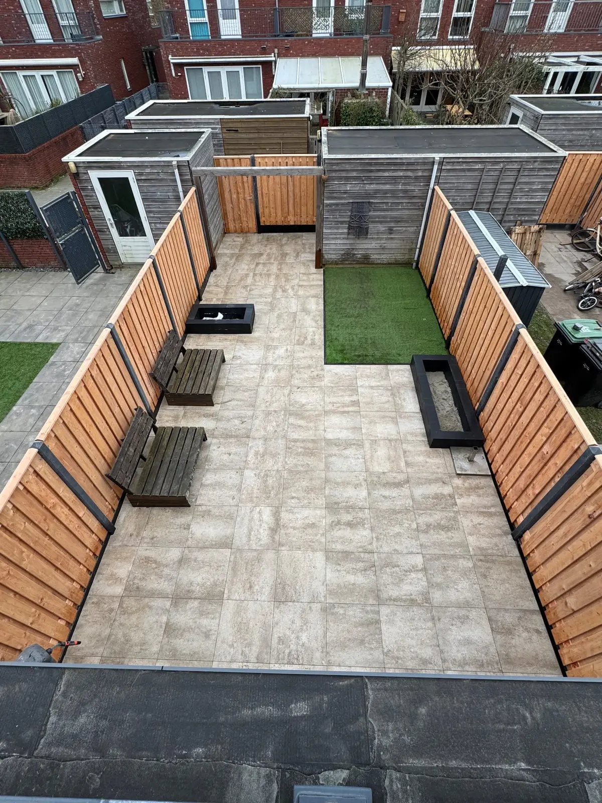 Tuin van bovenaf met terras, groen vlak en houten erfafscheiding