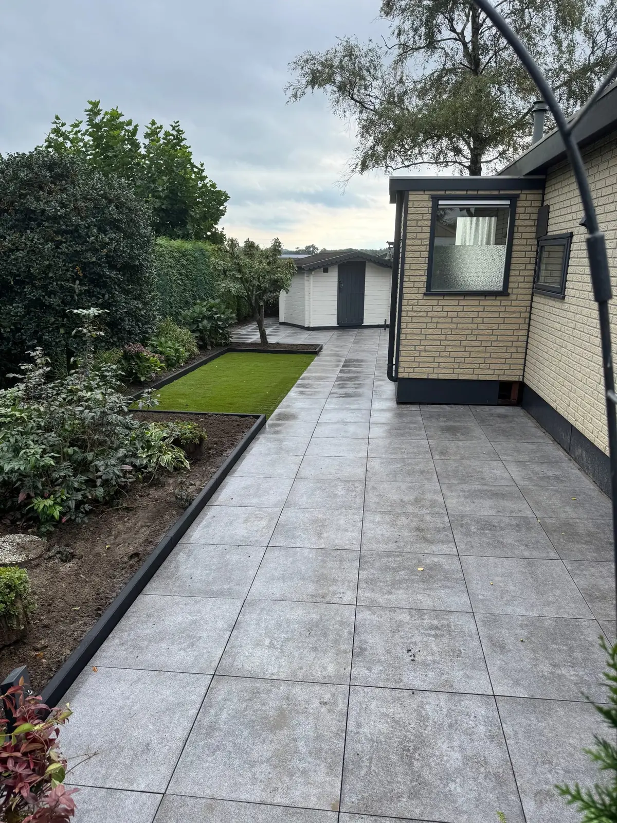 Bestrate looproute langs de woning met kunstgras en borders