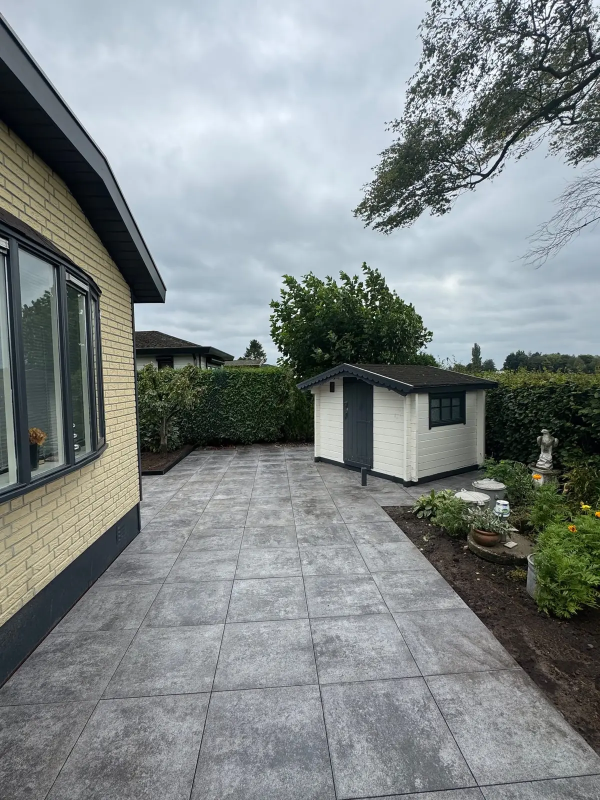 Groot betegeld terras tussen woning en berging in Voorthuizen