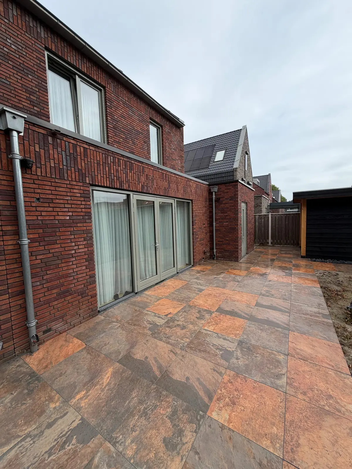 Nieuwe bestrating langs de achtergevel en glazen deuren