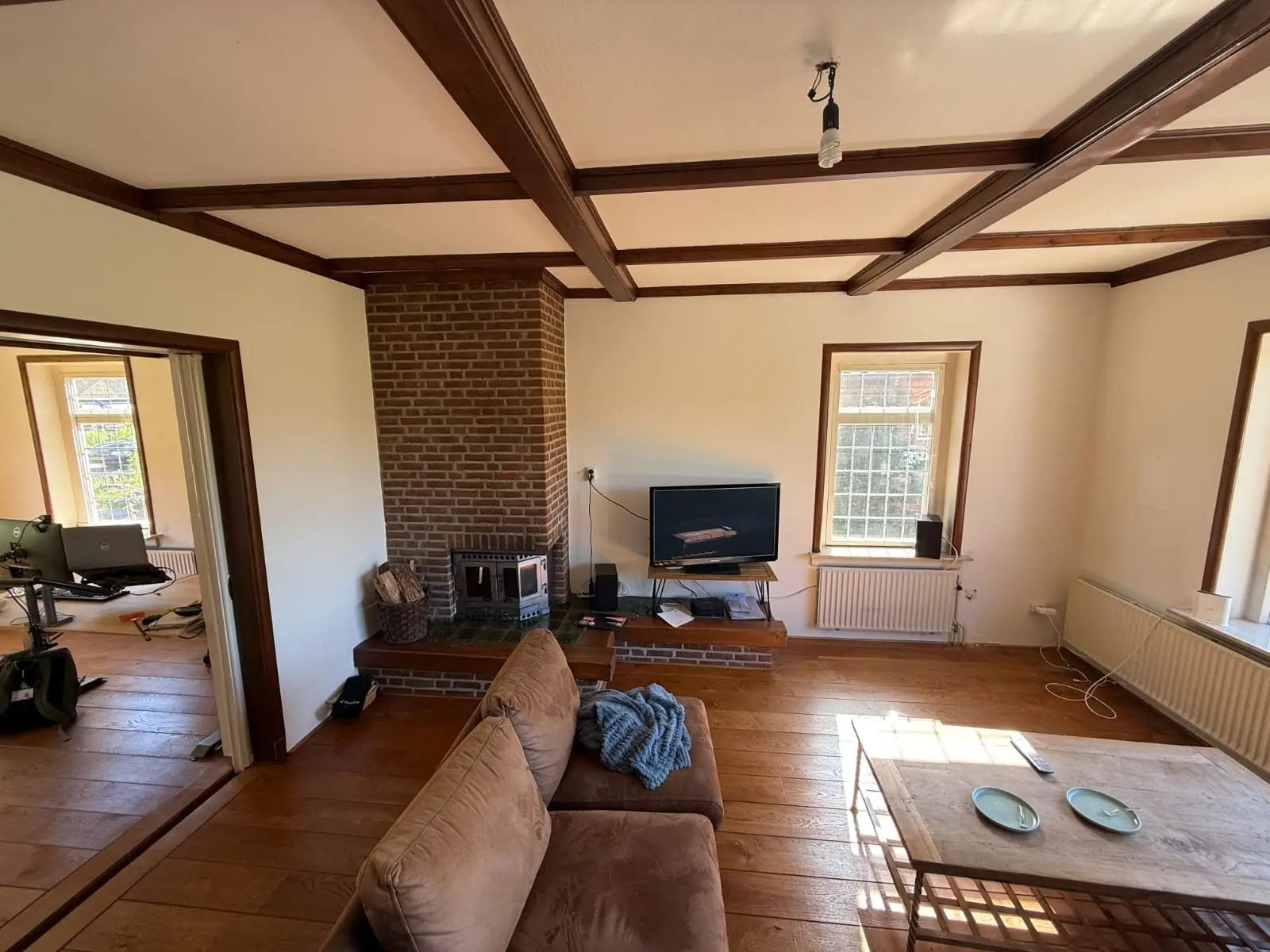 Woonkamer vóór de renovatie met balkenplafond en schouw